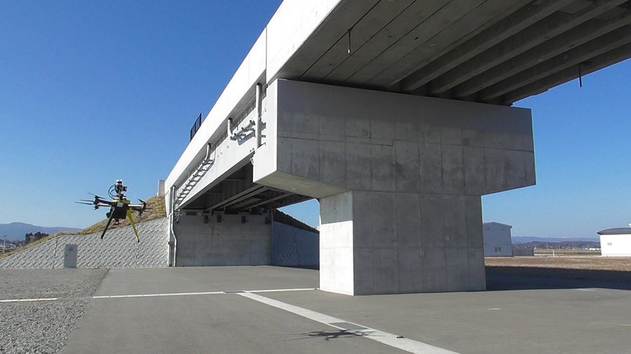 The underside and support structure of a concrete overpass, with a drone to the side on the left.